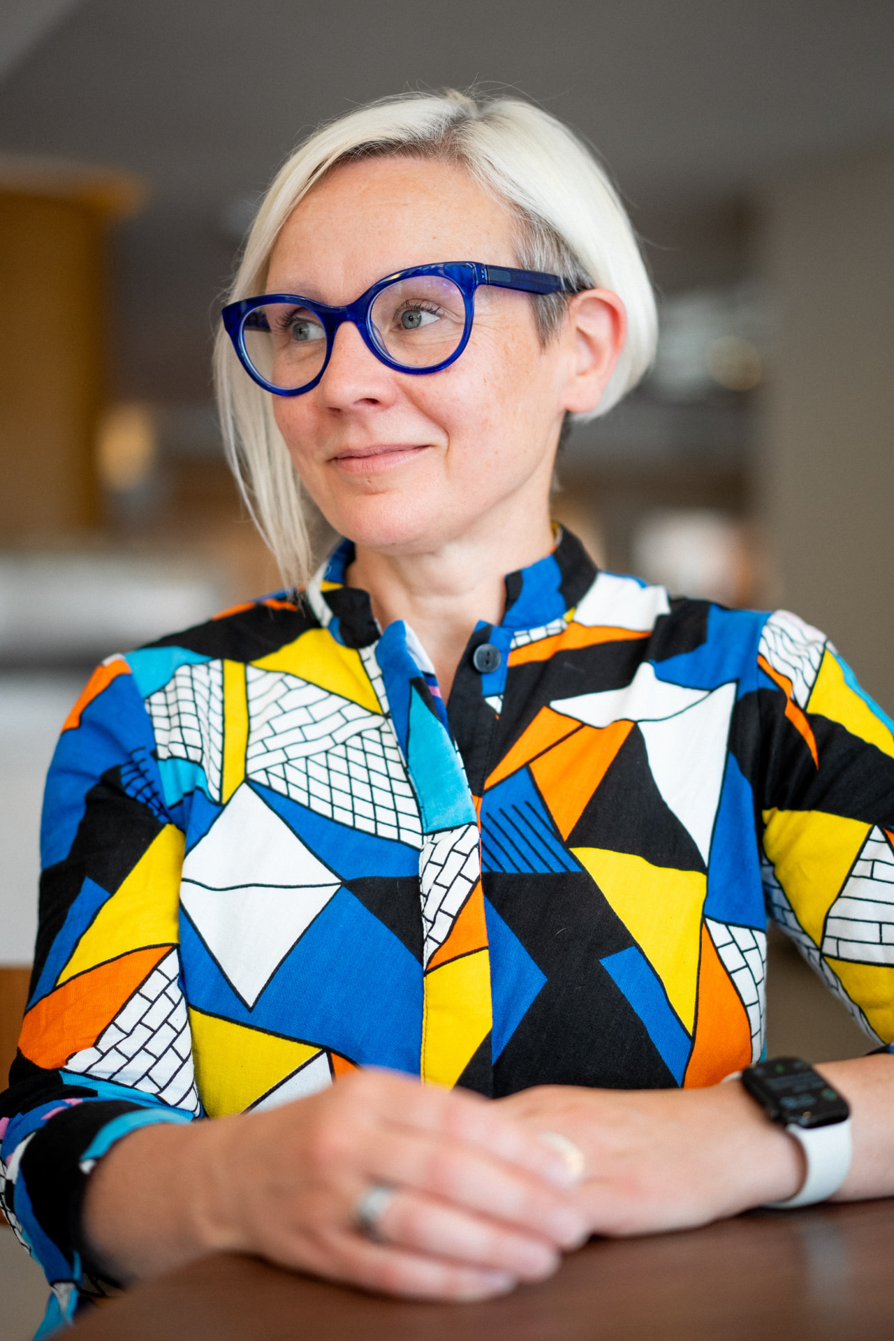 Lee Chalmers seated at a table, wearing blue glasses and a brightly patterned shirt.